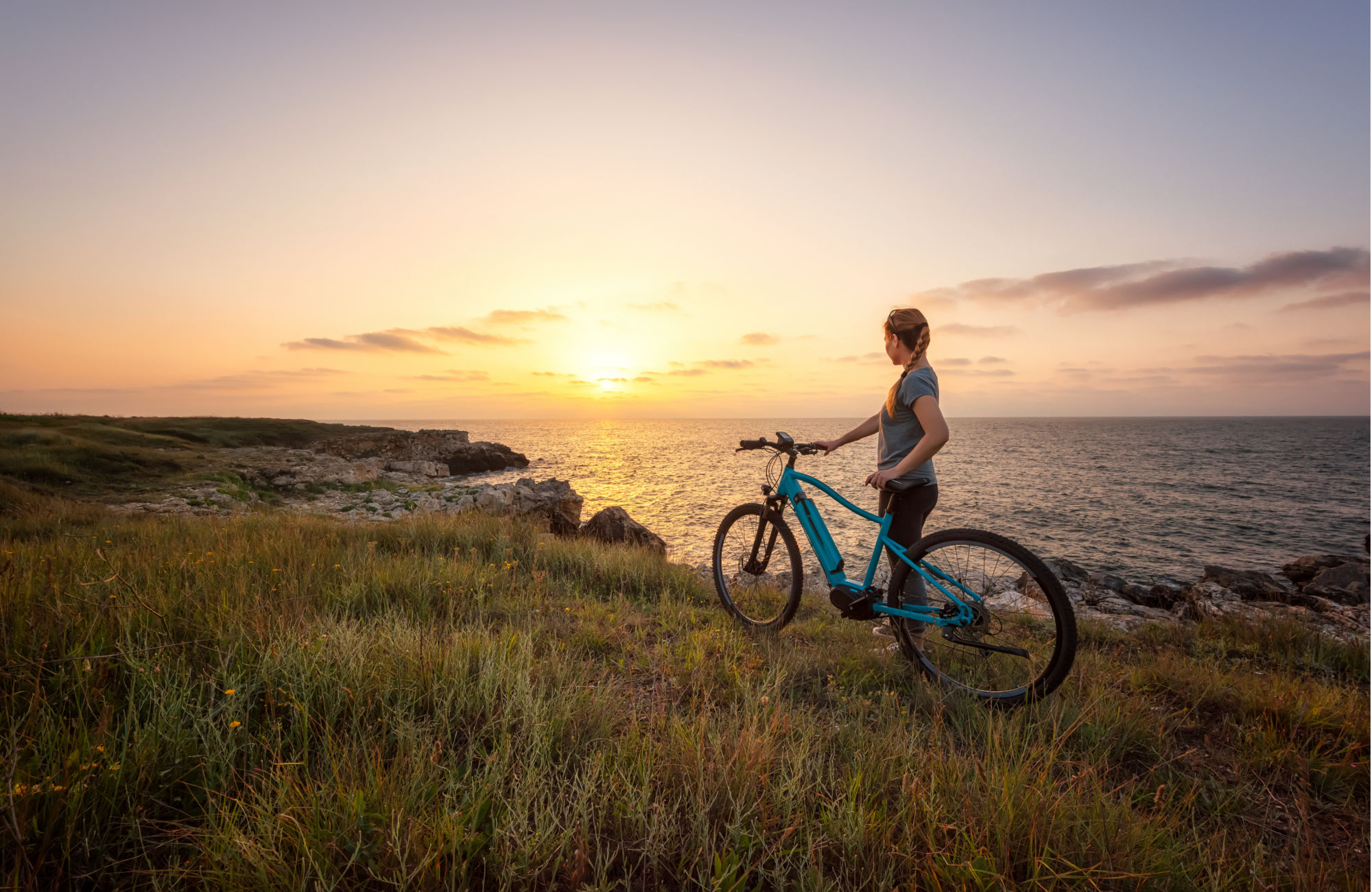 Ragazza che guarda un tramonto al mare con la sua bicicletta noleggiata da BikeandGo